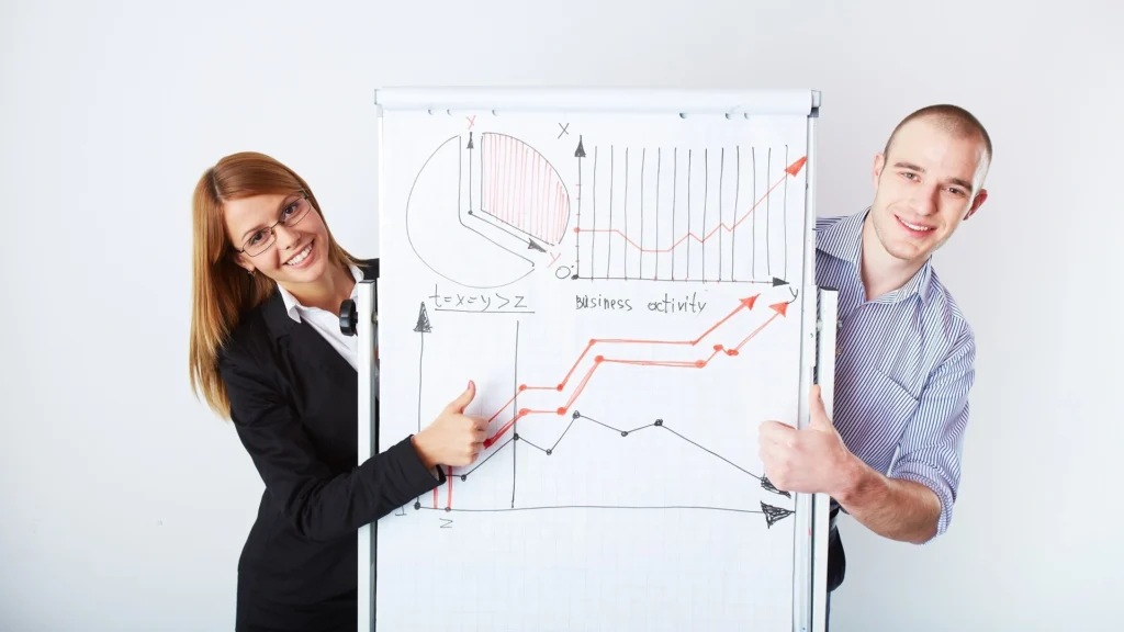 Deux professionnels présentant un tableau avec des graphiques et courbes de performance, illustrant le suivi des KPIs marketing