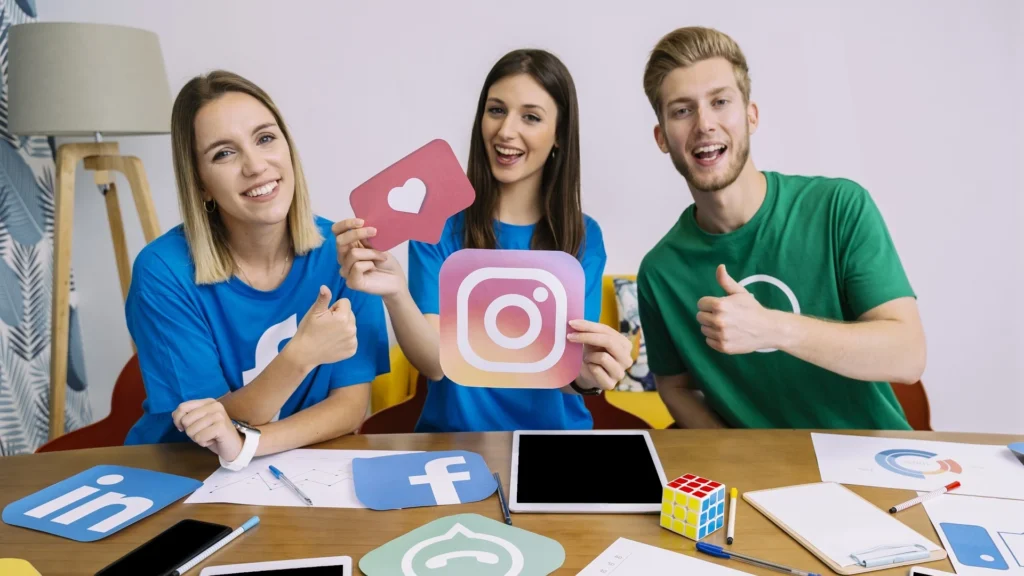 Jeunes marketeurs souriants tenant des logos de réseaux sociaux, illustrant une stratégie Meta Ads réussie